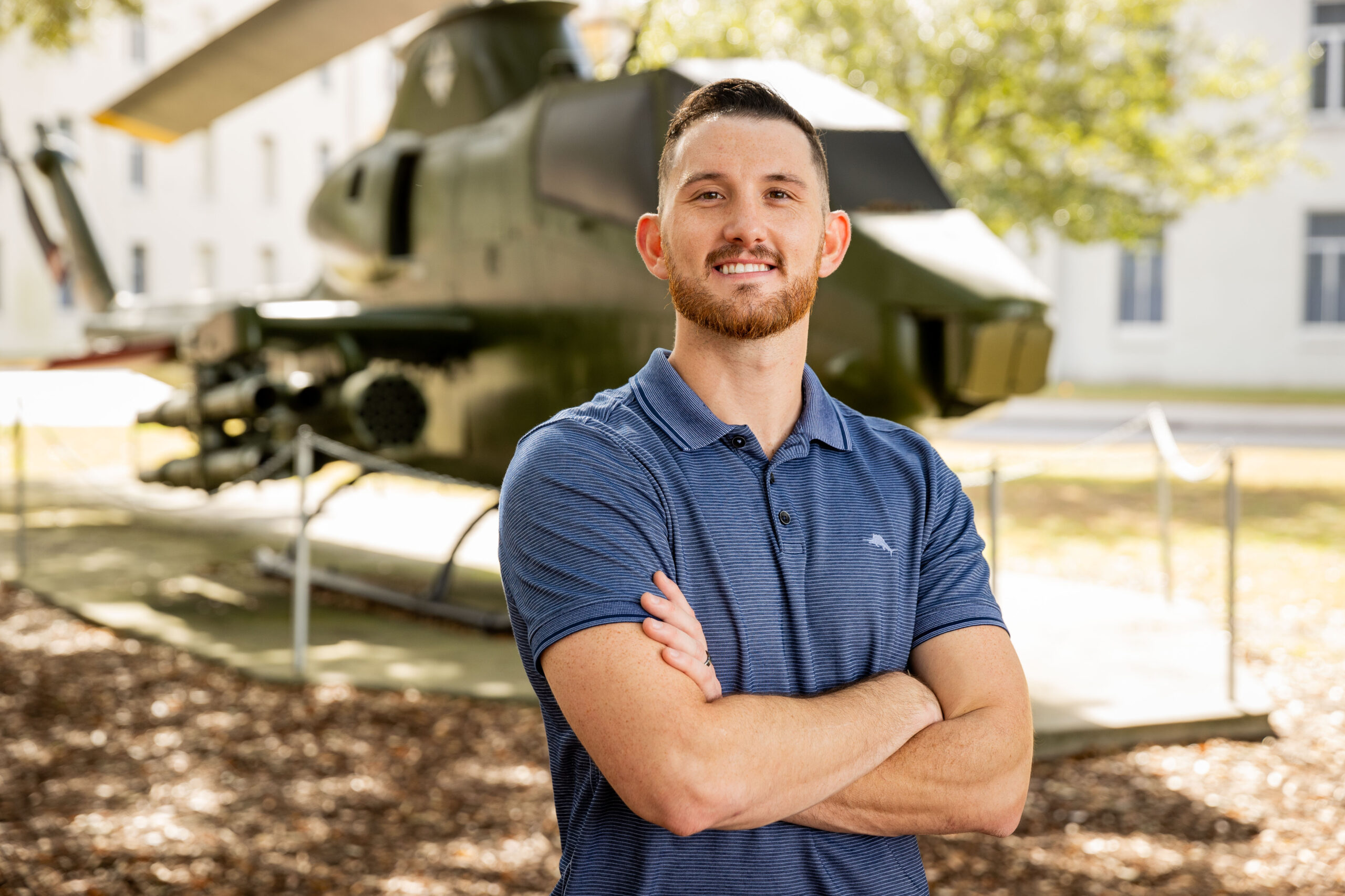 student stands with his arms crossed in front of a military helicopter on campus.