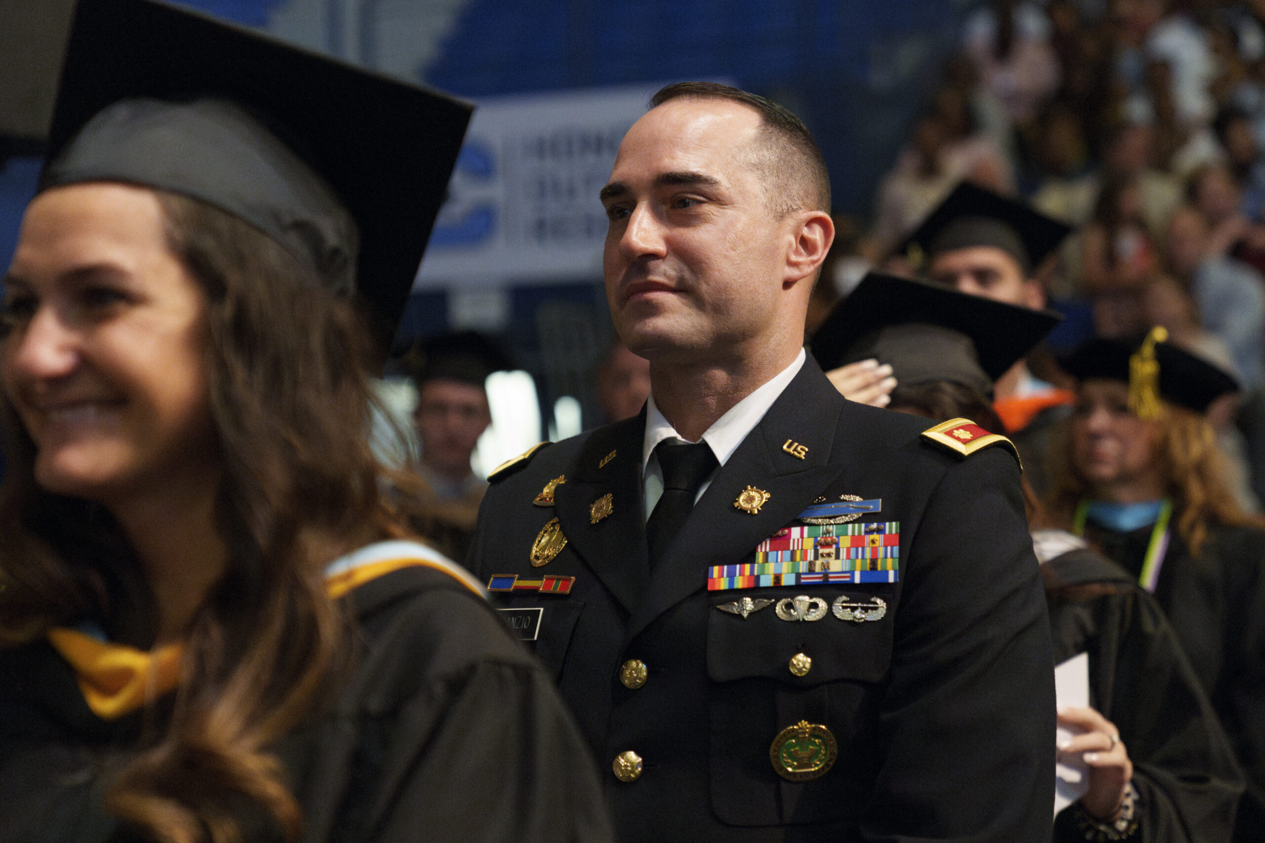 U.S. Army officer in dress uniform stands among graduates during a commencement ceremony.