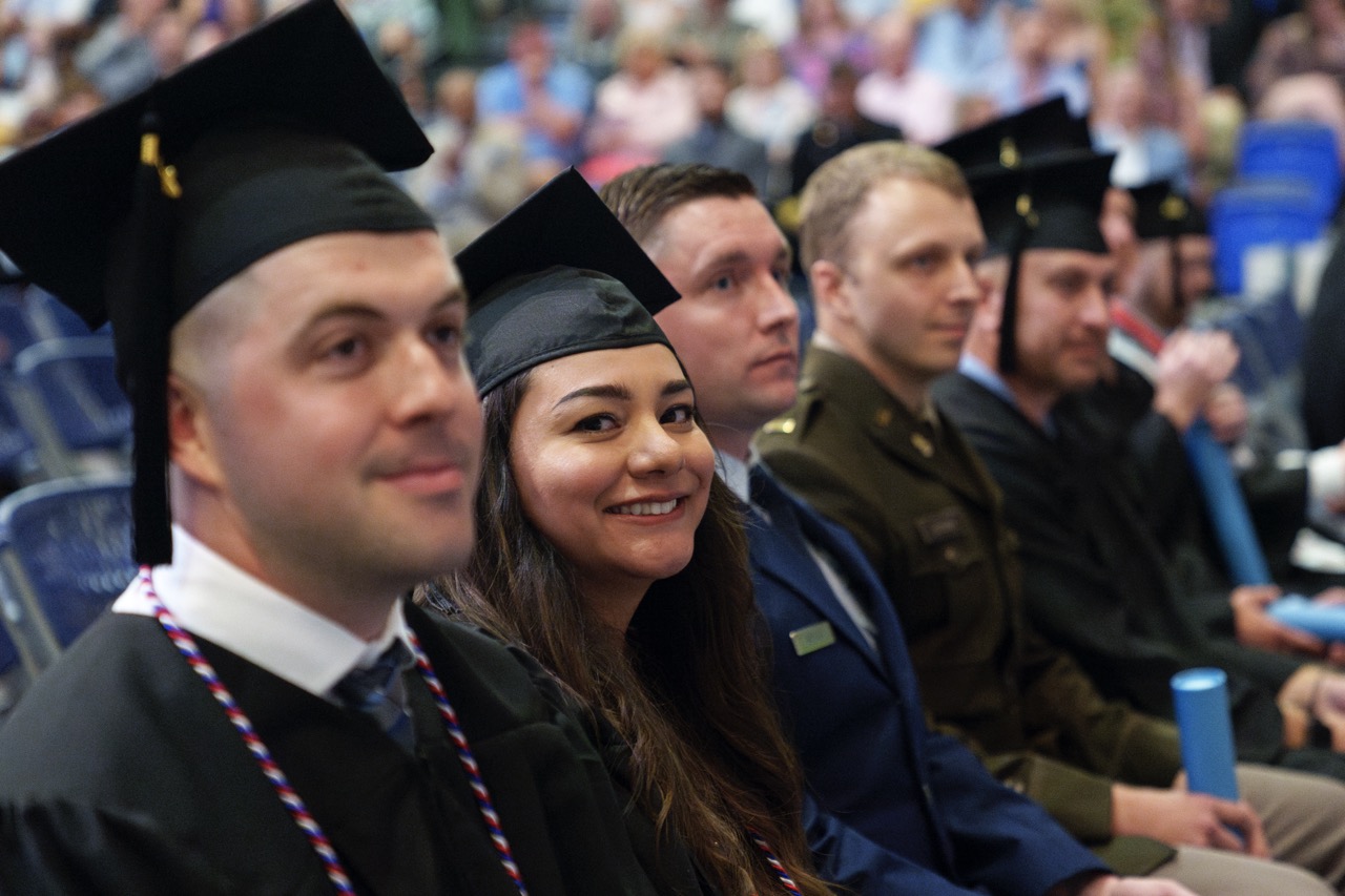 Graduates in caps and gowns sit together during a commencement ceremony.