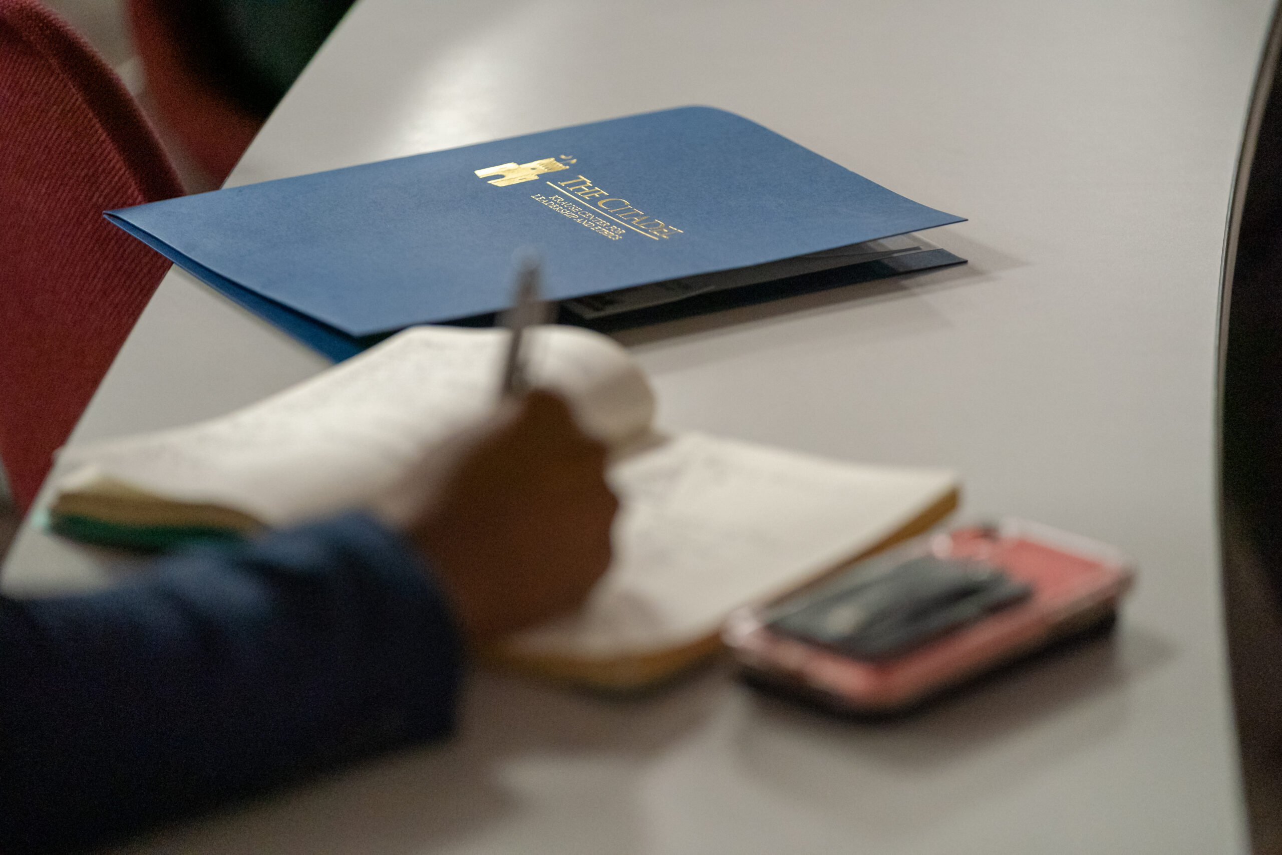 Student takes notes beside a folder bearing The Citadel logo.