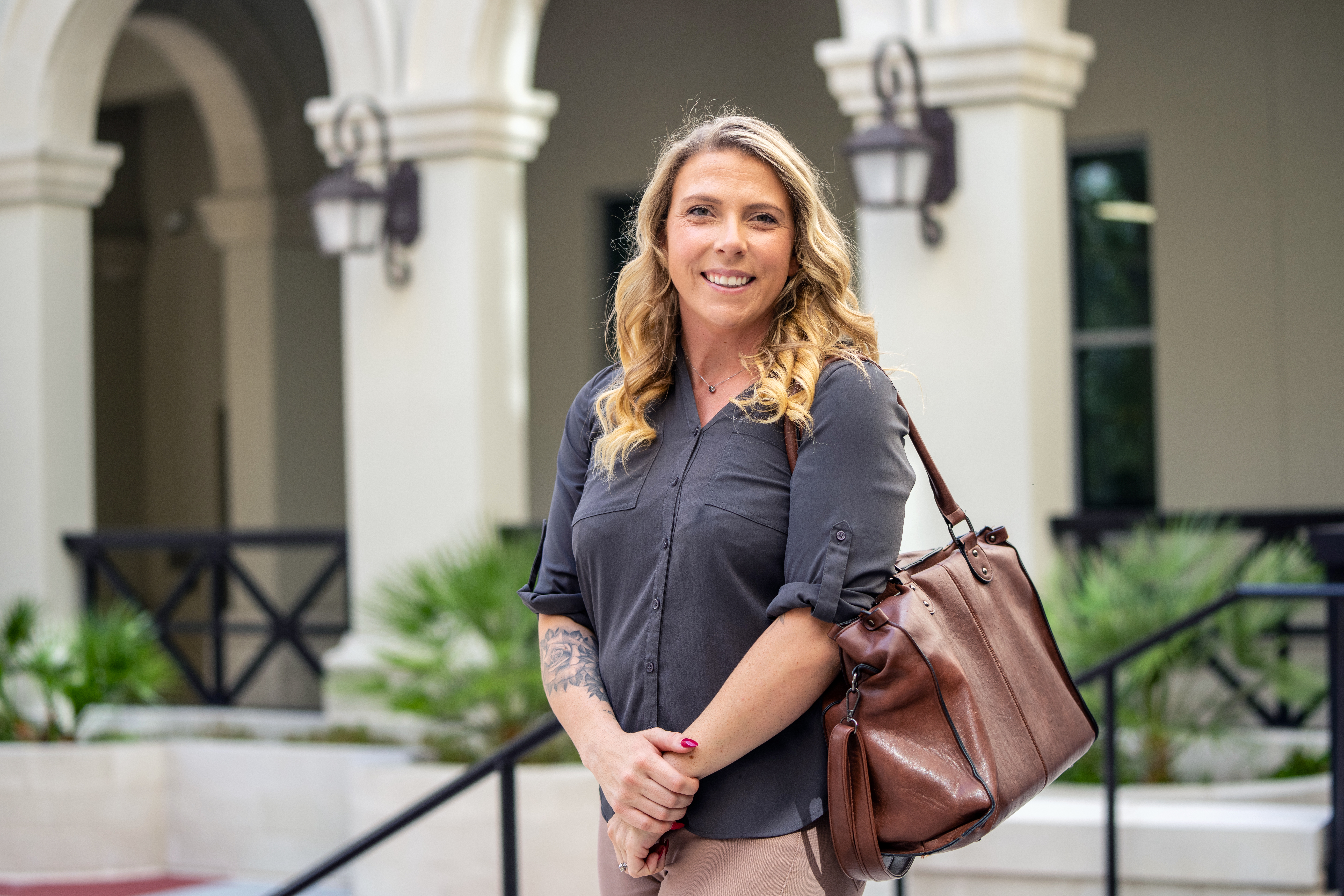 Woman carrying a shoulder bag stands outside a campus building.