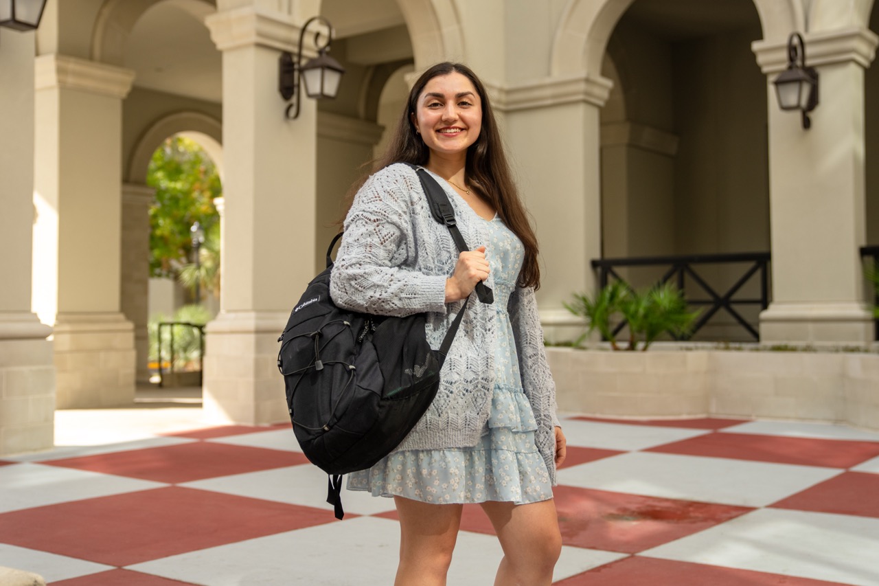 Student with a backpack stands in a campus courtyard.