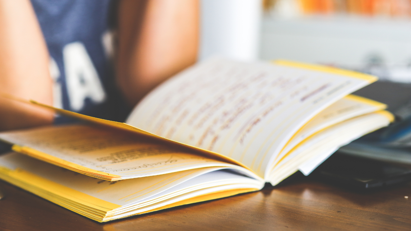 Open book resting on a table with a person reading in the background.