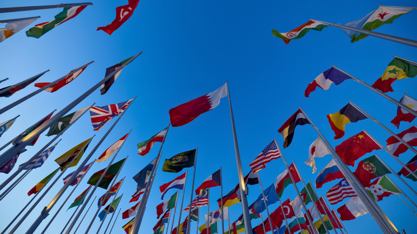 International flags flying on flagpoles against a clear blue sky.
