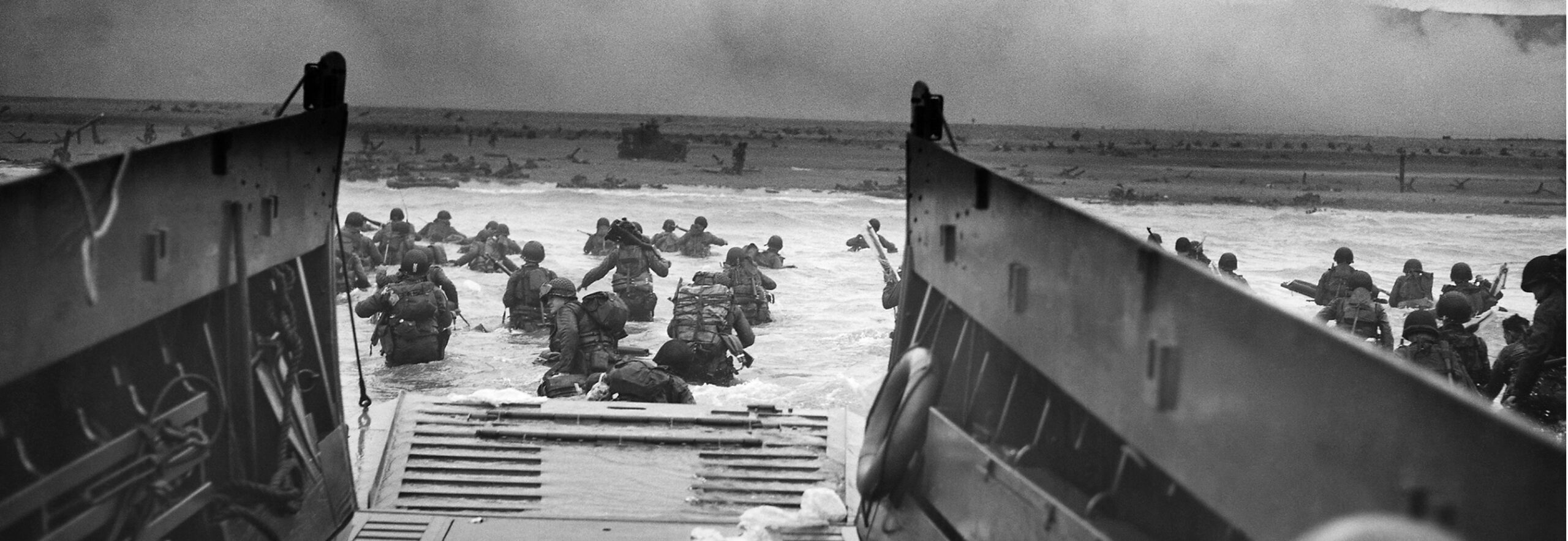 Black-and-white photograph of soldiers wading ashore from a landing craft during the Normandy invasion.