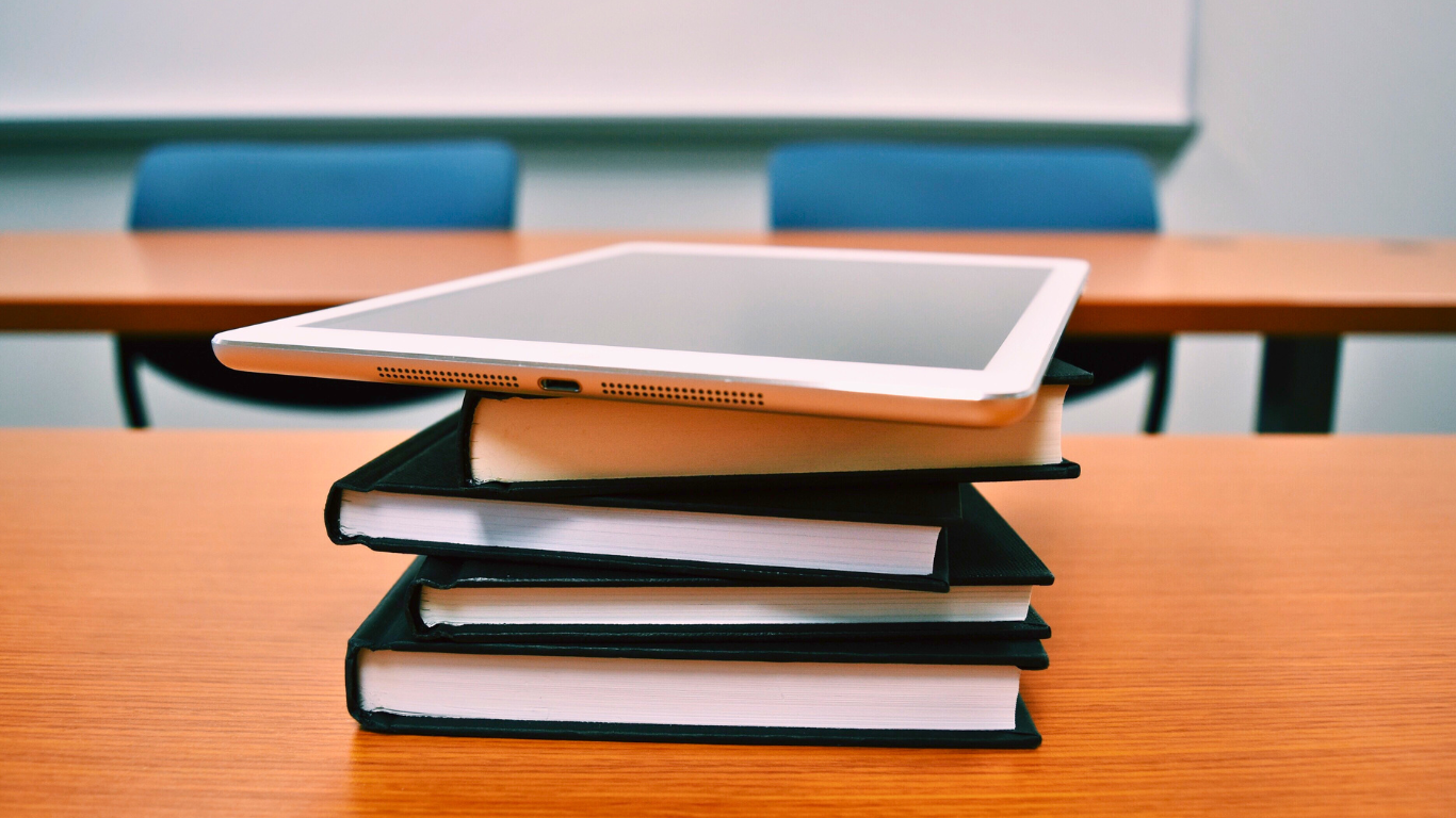 Tablet rests on a stack of books on a classroom desk.