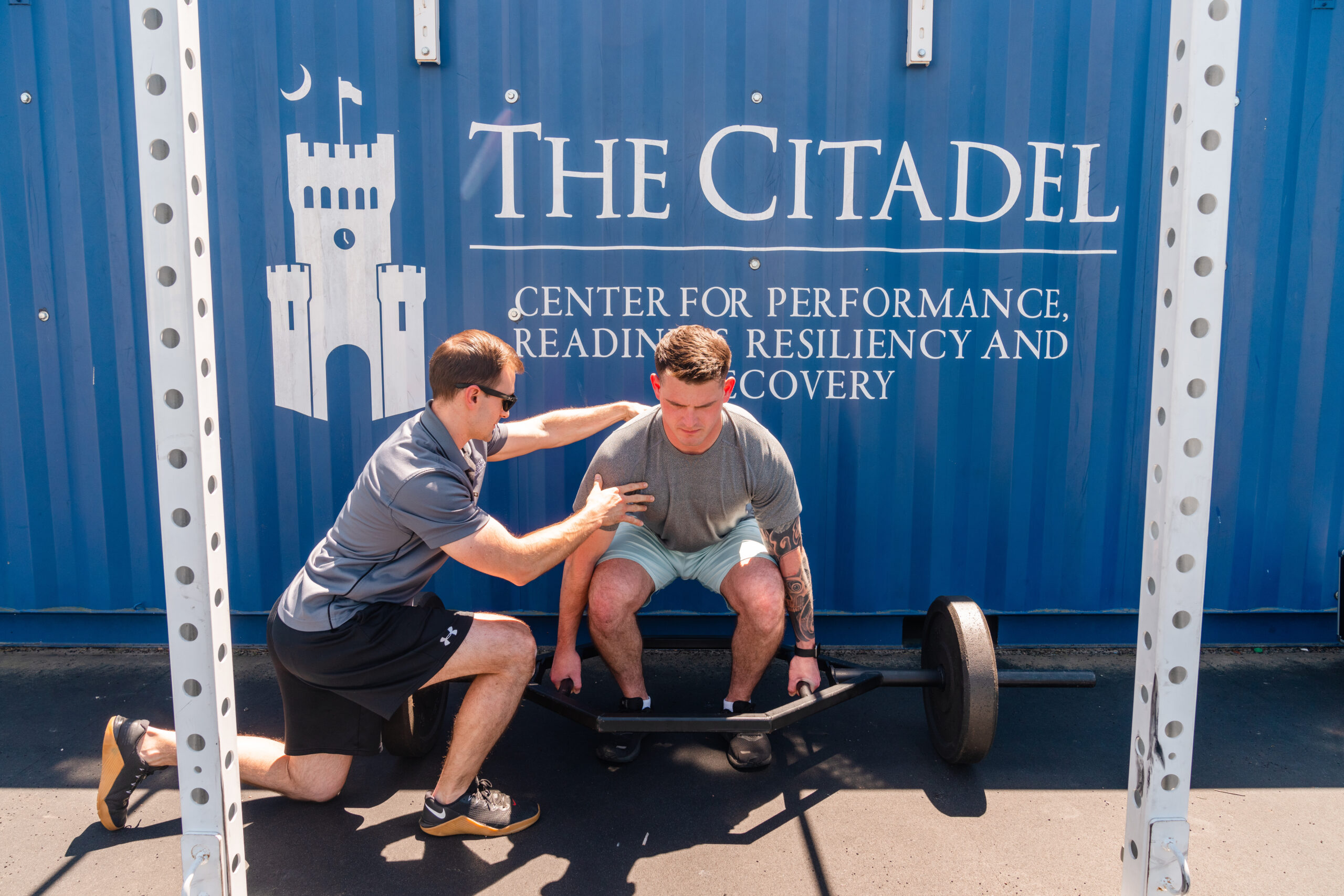 Trainer assists a man preparing to lift weights outside The Citadel Center for Performance, Readiness, Resiliency and Recovery.