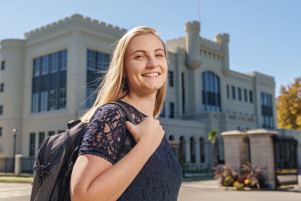 Female student with a backpack smiles outside a campus building.