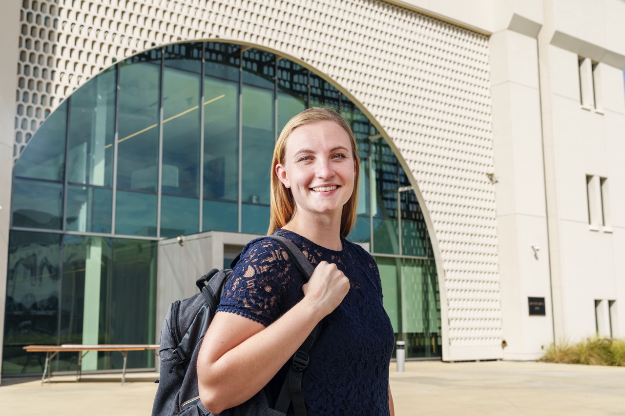Female student with a backpack smiles outside a campus building.
