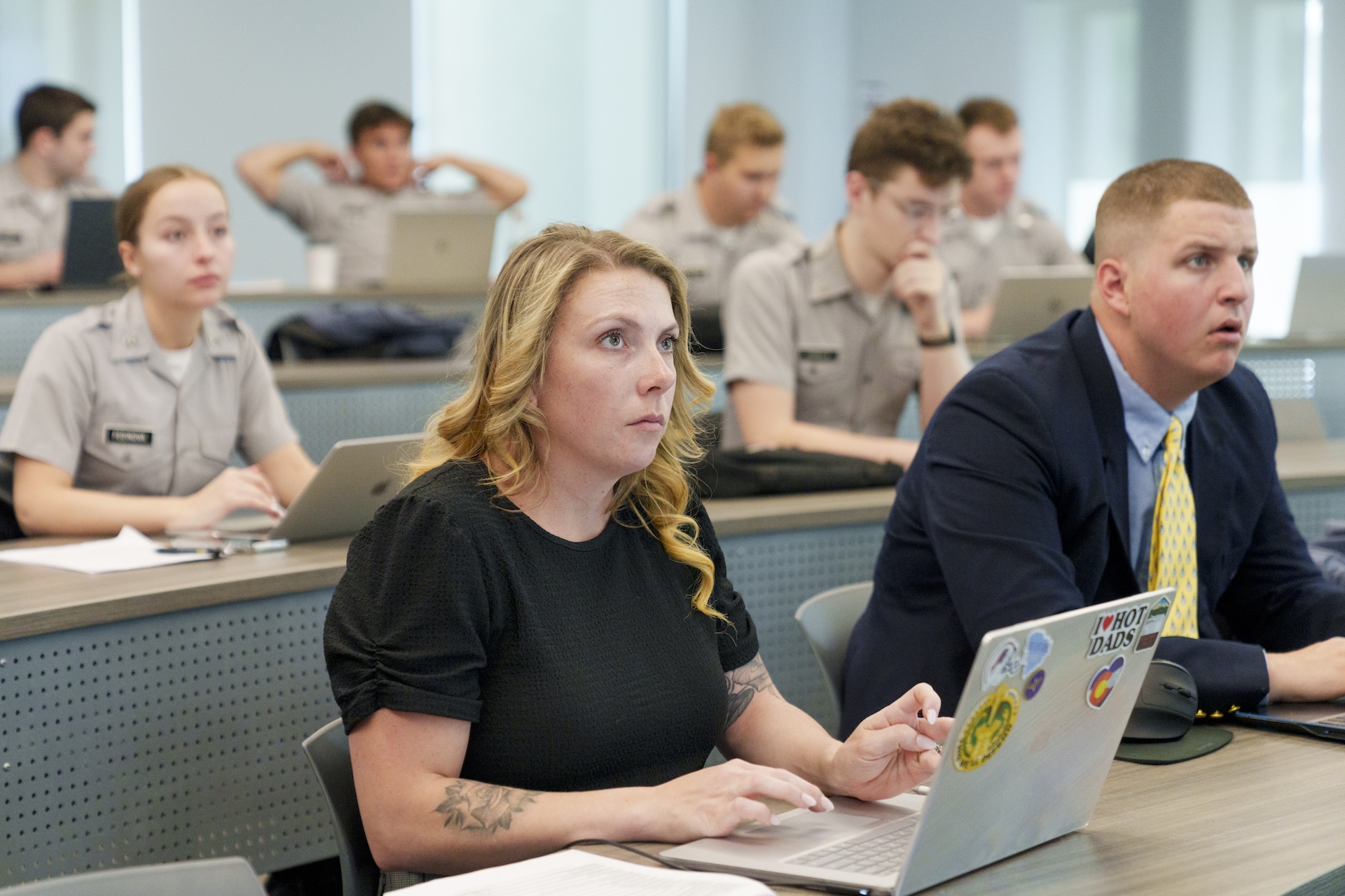 Students and veteran students work on laptops during a classroom lecture.