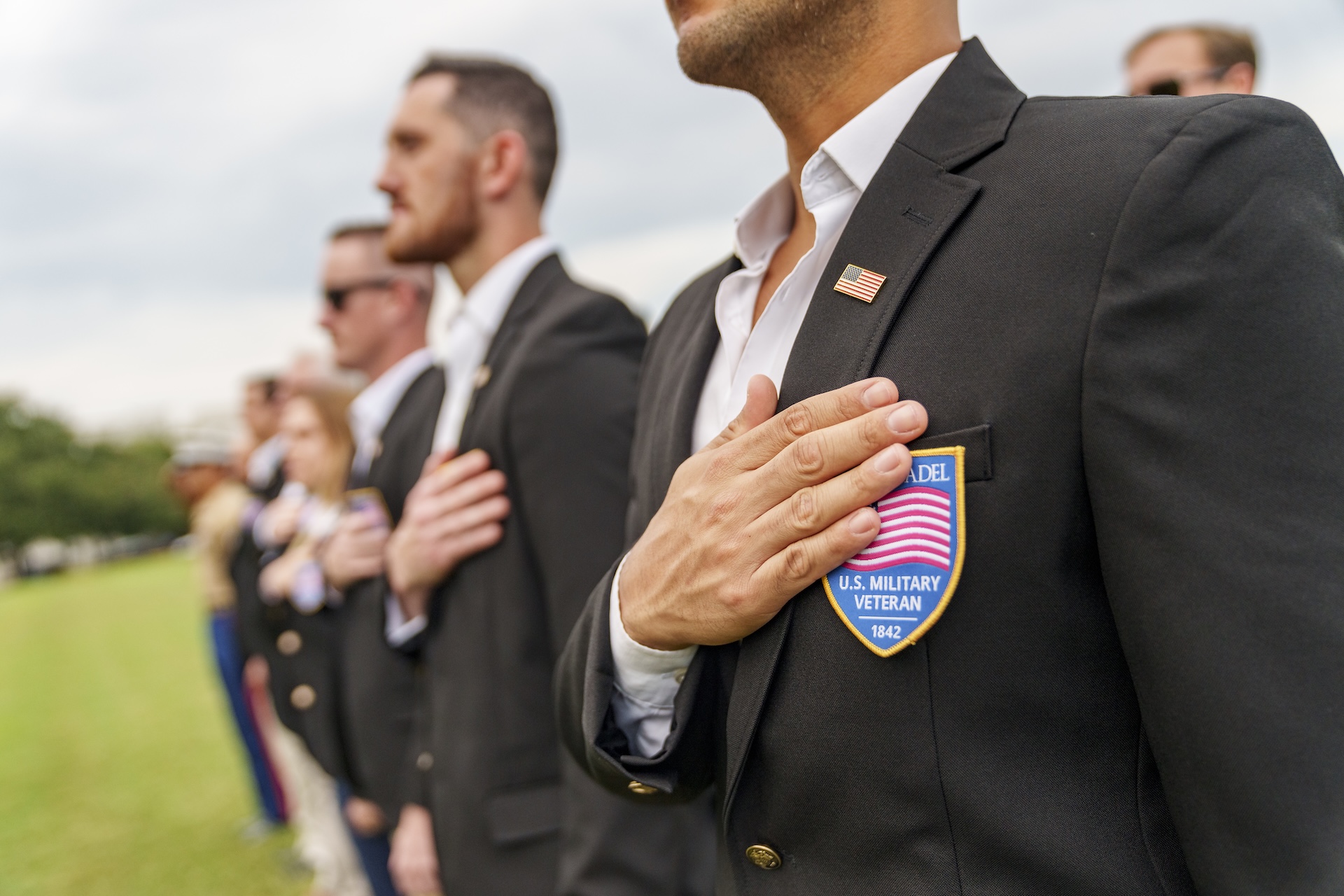 Military veterans wearing Citadel blazers place their hands over their hearts during a ceremony.