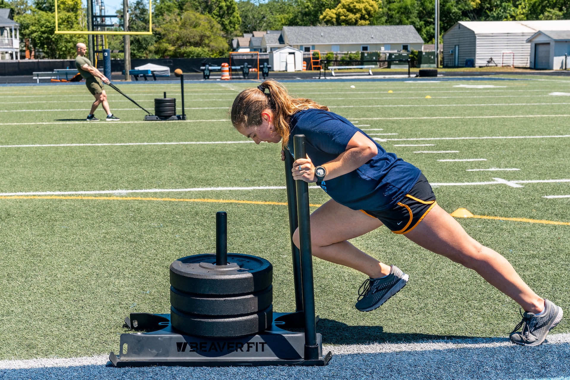 Student pushes a weighted training sled across an athletic field.