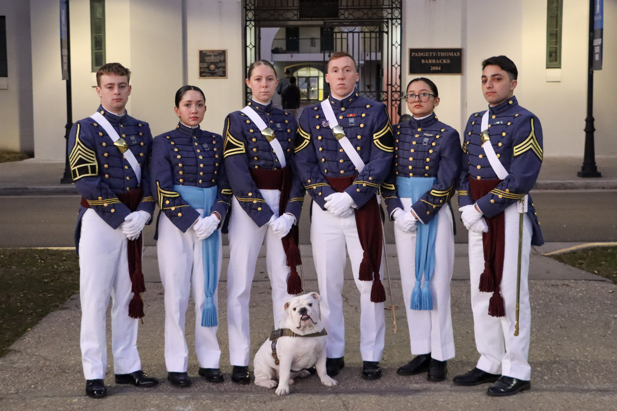 Six cadets in dress uniforms pose with a bulldog outside Padgett-Thomas Barracks.