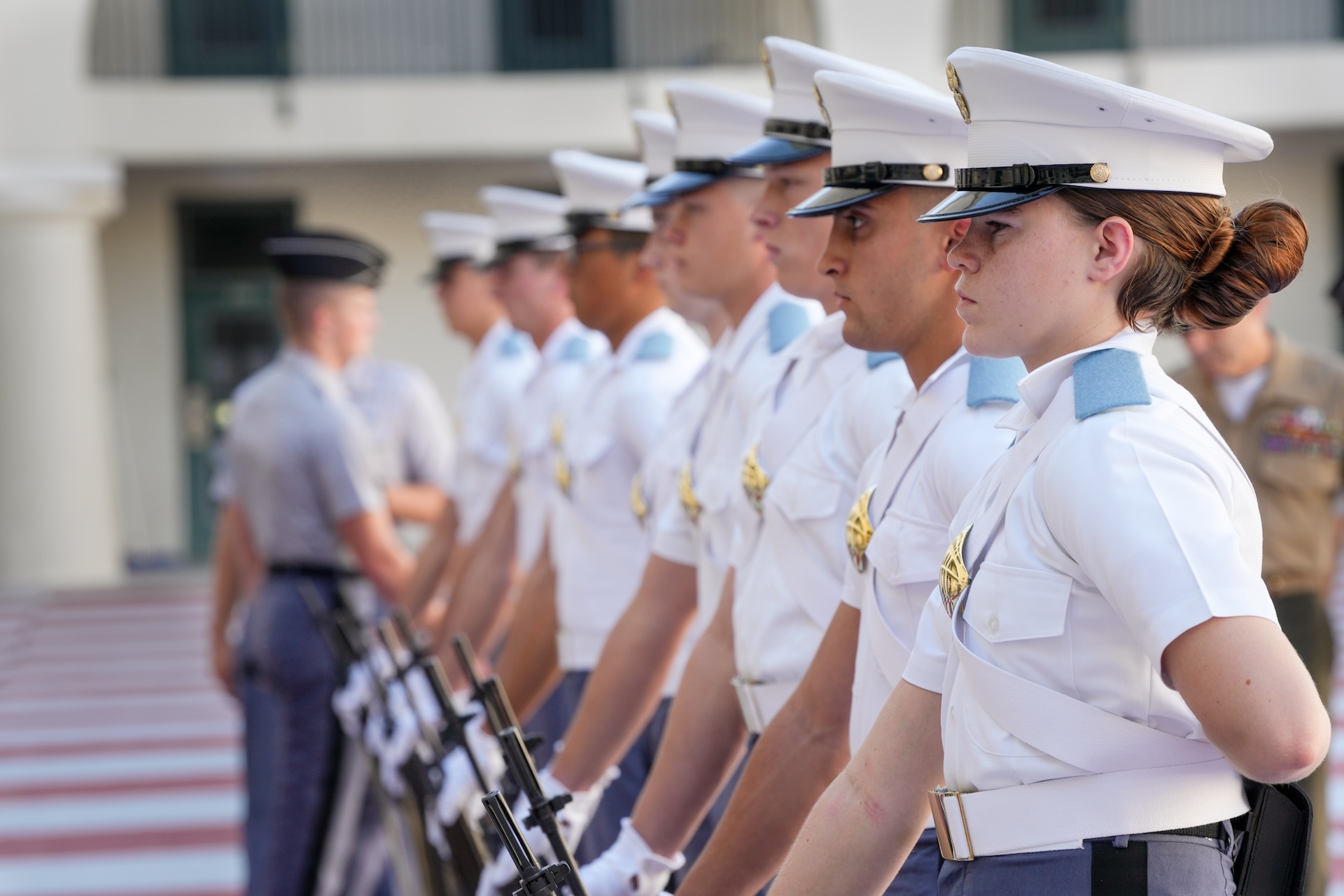 Cadets in white uniforms stand in formation during an inspection in a barracks courtyard.