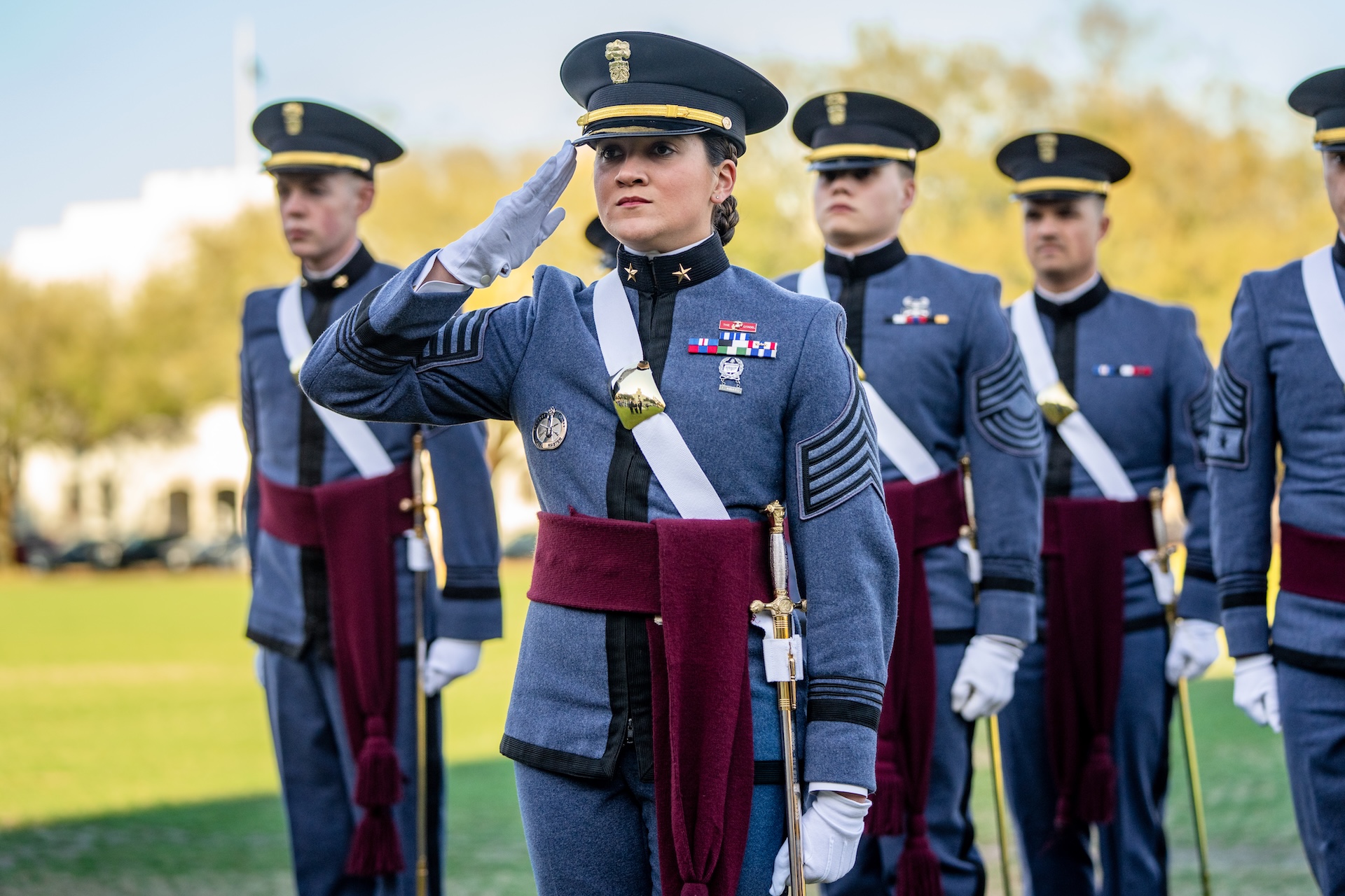 Citadel cadet in dress uniform salutes while standing in formation outdoors.
