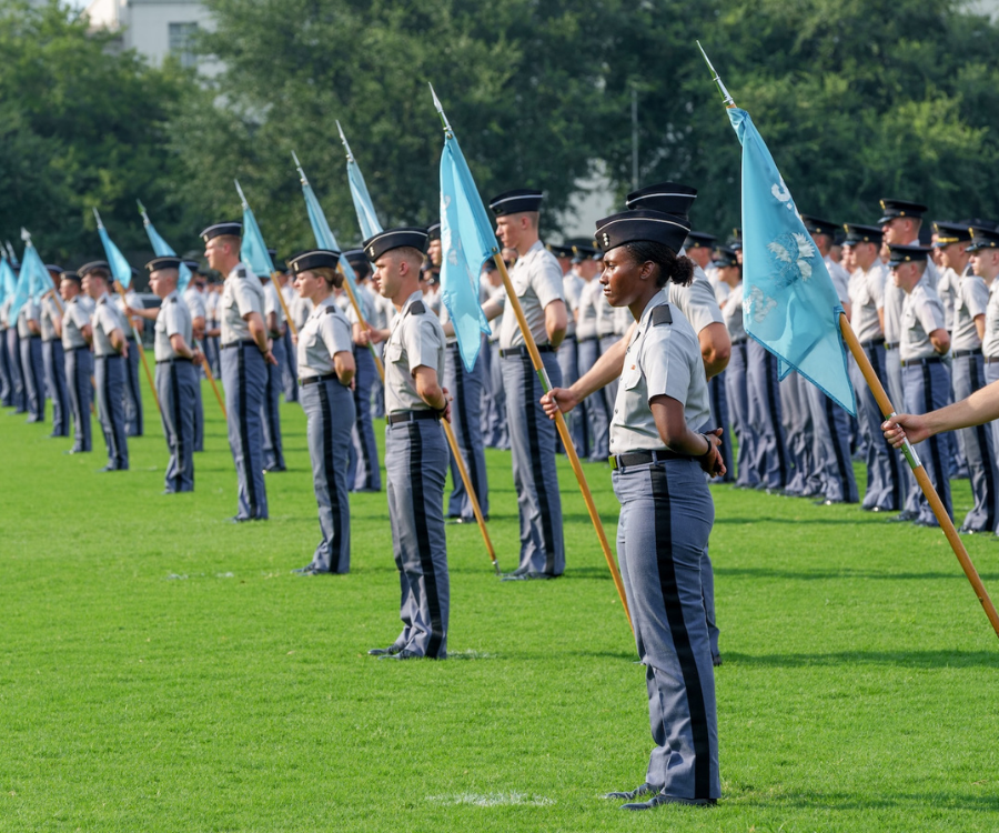 Cadets stand in formation on Summerall Field holding light blue company guidons.