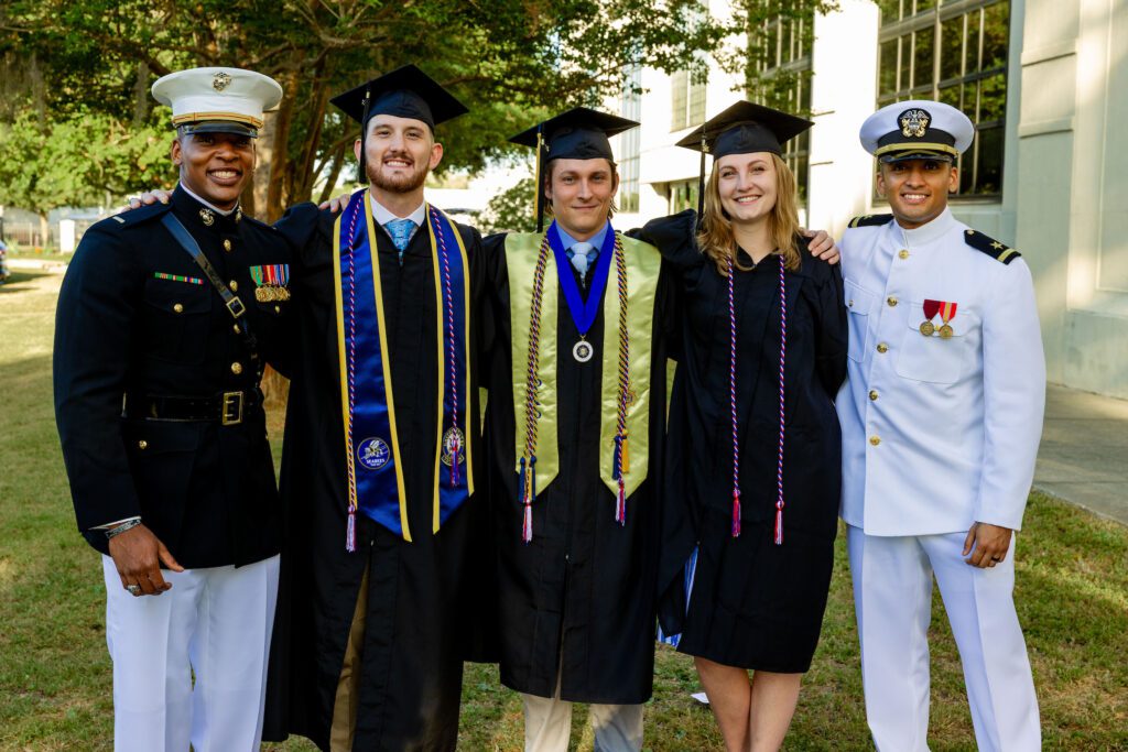 Graduates and military service members pose together outdoors following commencement.