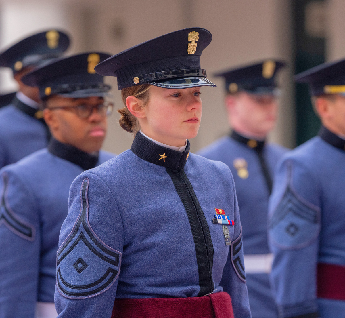 Close-up of a cadet in white dress uniform standing at attention during a parade ceremony, with other cadets in formation in the background